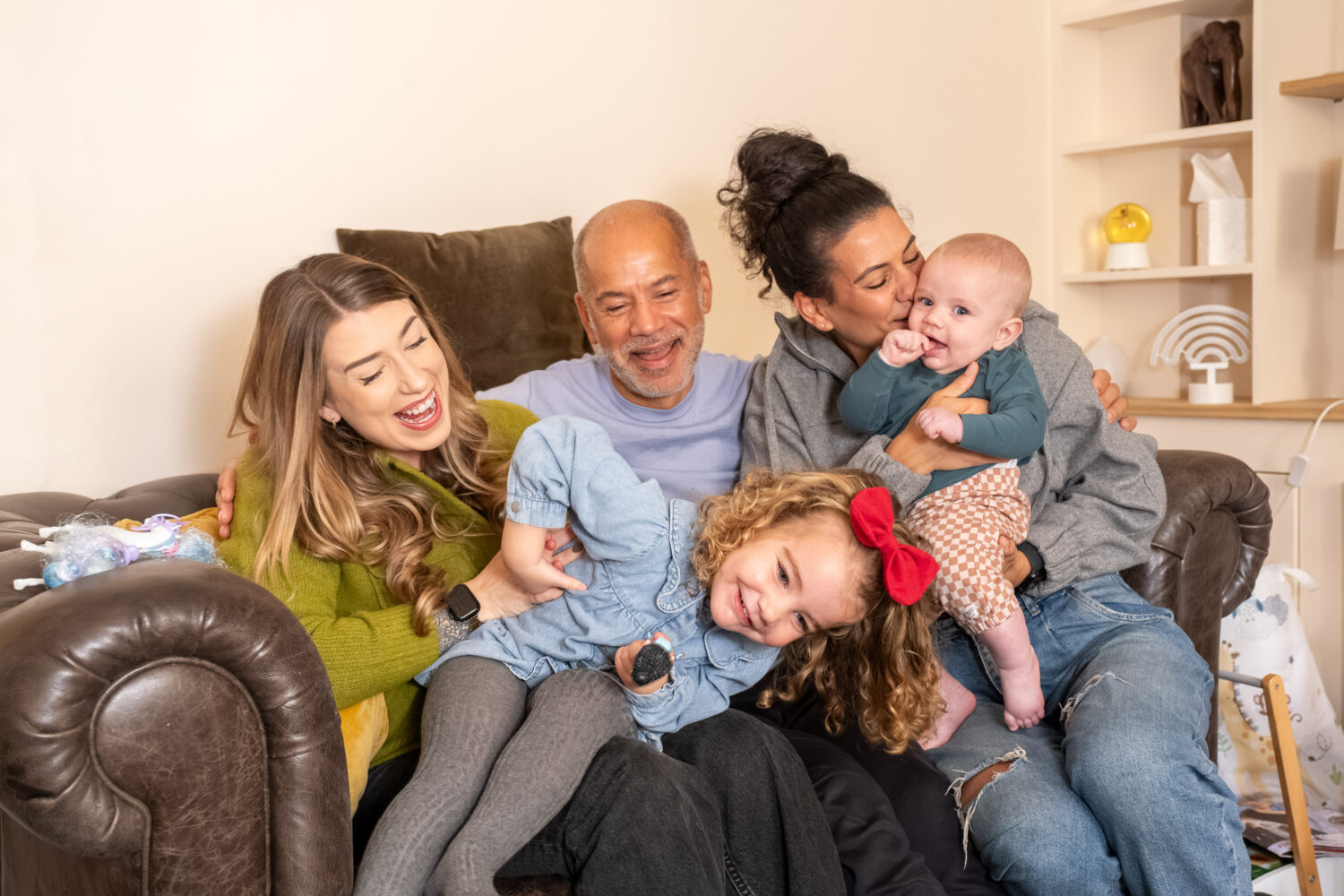 A family with three adults and two children laugh and embrace on a sofa
