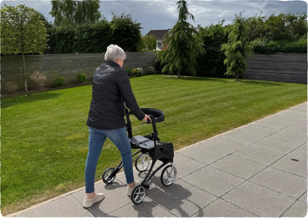 A lady walks in a garden using a walking aid
